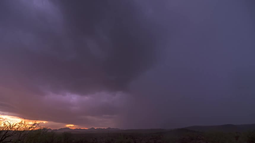 An ominous purple thunderstorm flashes with lightning over a desert landscape during a dramatic sunset