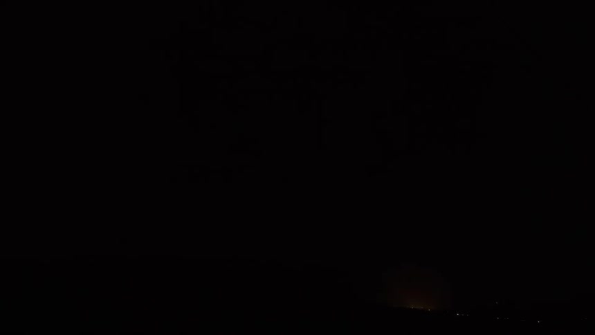 A powerful lightning storm illuminates the night sky with brilliant flashes over a distant city and mountains