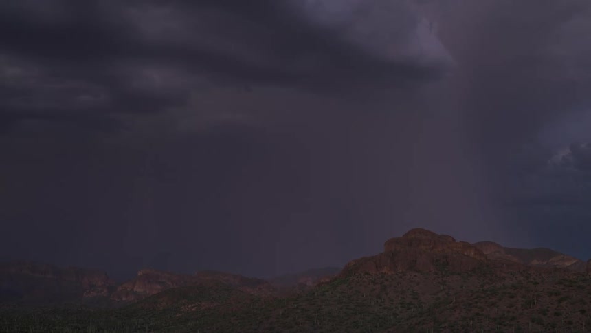 A powerful lightning storm erupts over a desert mountain range at dusk, illuminating the dark sky