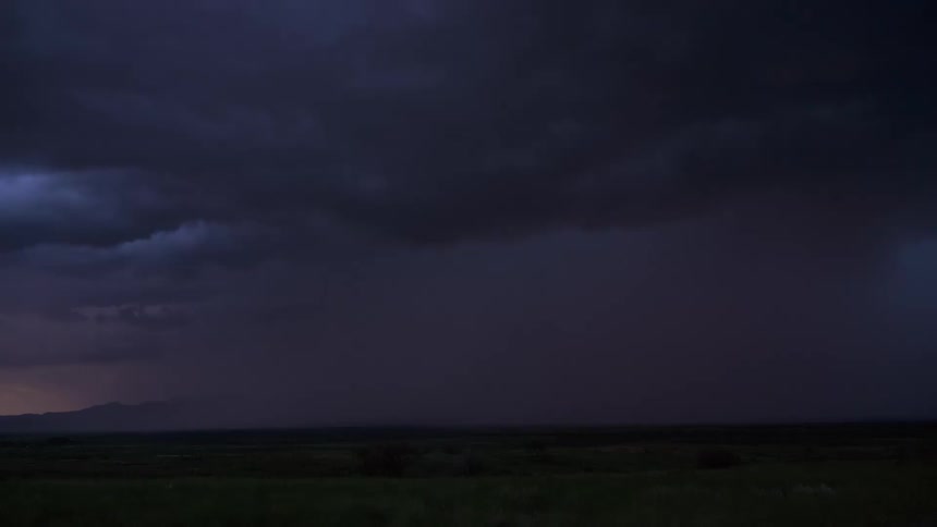 A powerful time-lapse of a dramatic lightning storm with frequent strikes illuminating the purple night sky over a vast, grassy plain