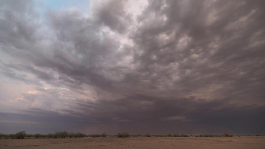 A dramatic timelapse of ominous storm clouds gathering and rolling over a vast desert landscape at dusk