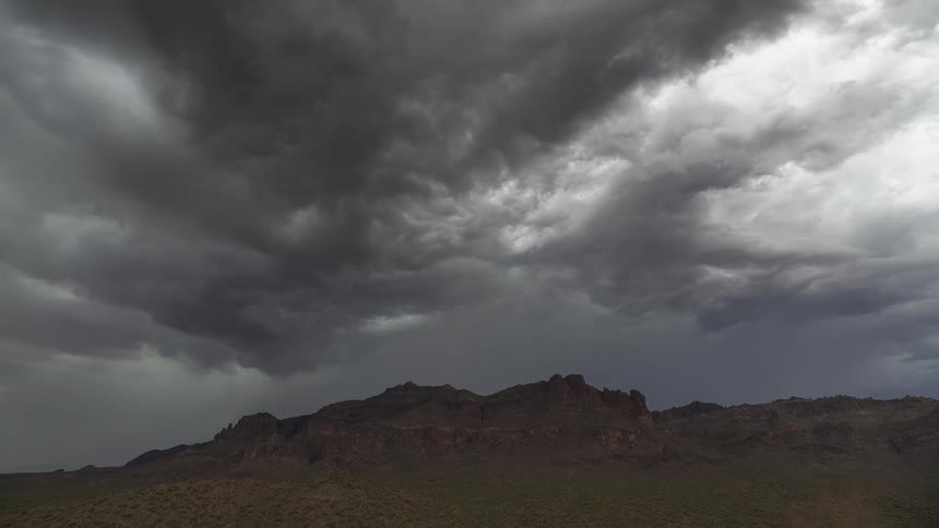 Ominous storm clouds gather over a rugged mountain landscape in the desert