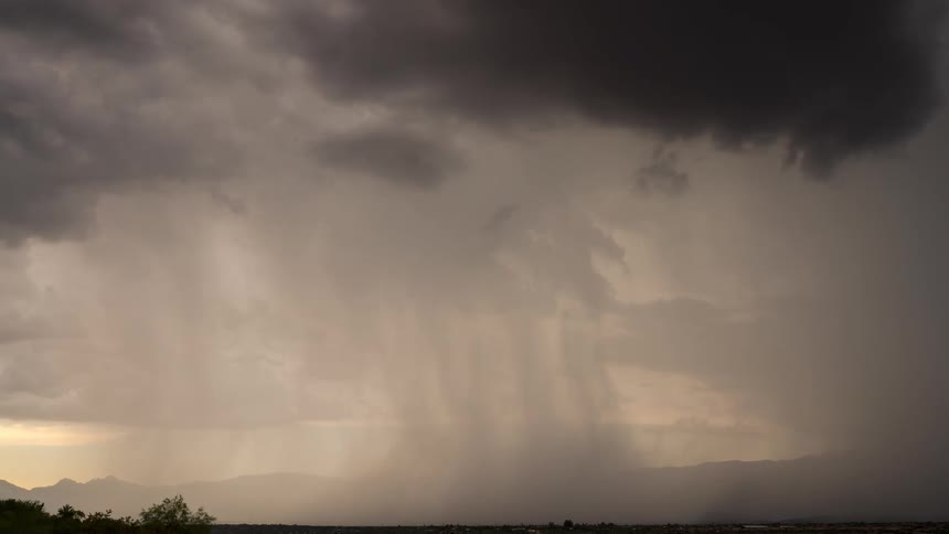 Dramatic dark storm clouds release a heavy downpour over a valley landscape