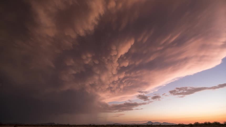 An awe-inspiring timelapse of a massive mammatus storm cloud formation glowing with orange and pink hues over the desert at sunset
