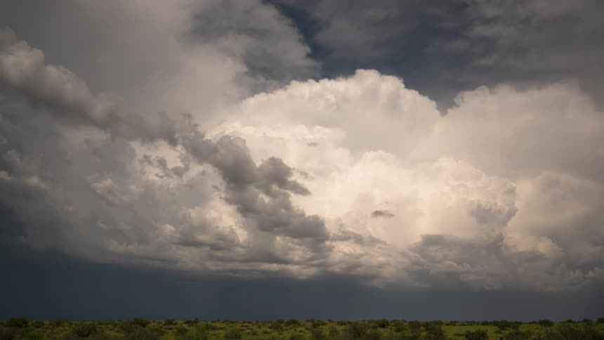 A dramatic time-lapse captures a massive storm cell with boiling cumulonimbus clouds growing over a vast, green landscape