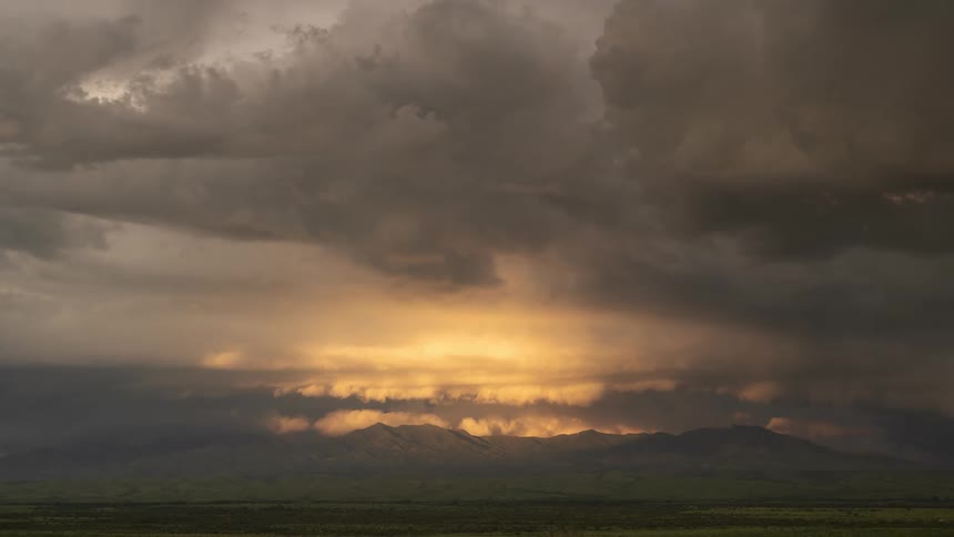 Golden sunlight breaks through dramatic storm clouds over a distant mountain range in a beautiful time-lapse