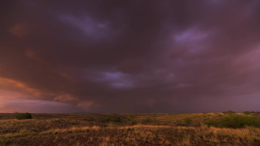 Dramatic storm clouds glow with fiery orange sunset light before turning purple and unleashing lightning over a vast landscape