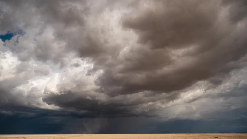 A dramatic time-lapse of a powerful dust devil swirling across the desert landscape under a turbulent, stormy sky