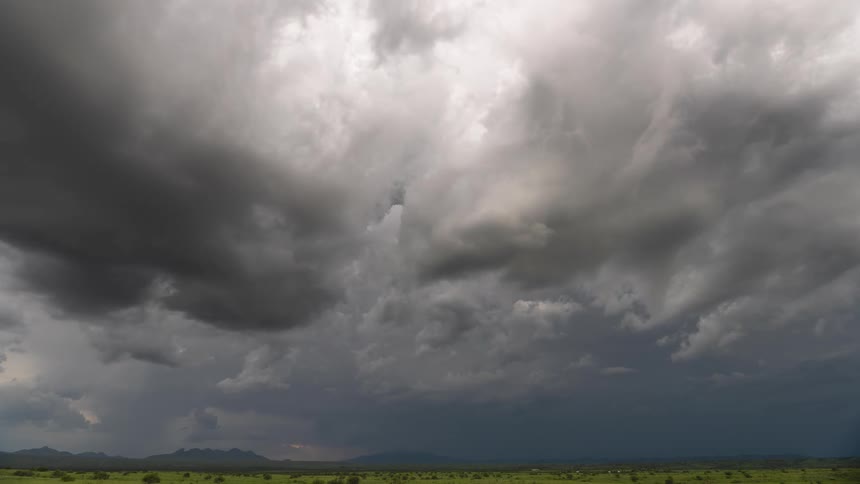 Dark, swirling storm clouds gather over a vast, green landscape, creating a dramatic and ominous scene