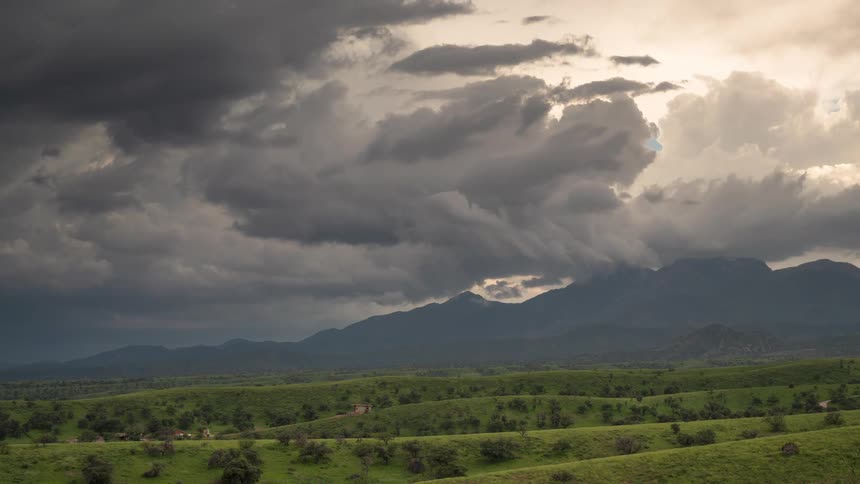 A dramatic time-lapse of dark, turbulent storm clouds moving over a lush green mountain valley