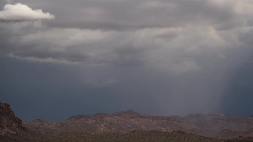 A dramatic rain shaft falls from heavy storm clouds over a vast and rugged mountain range