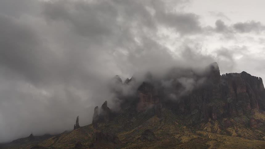 Ominous storm clouds slowly roll over the peaks of a rugged desert mountain