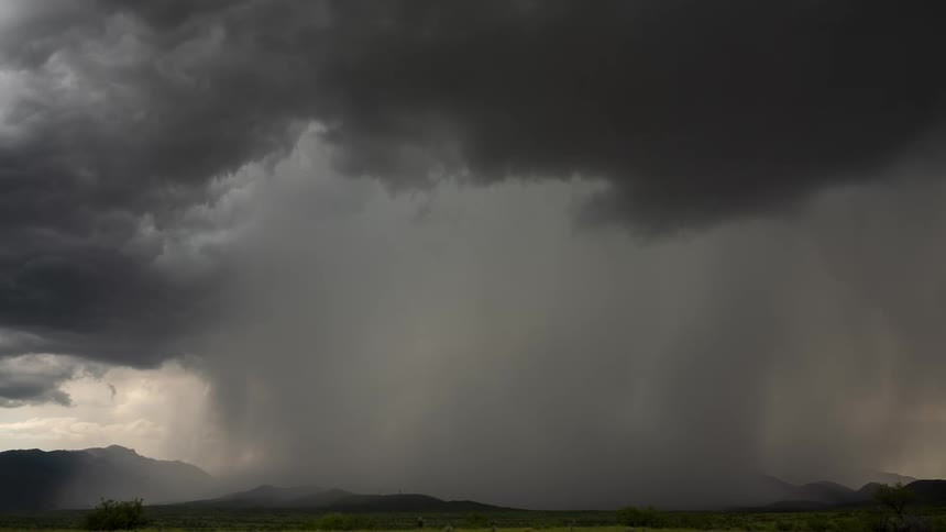 A dramatic time-lapse captures a powerful thunderstorm moving across a mountain landscape, unleashing a torrential downpour