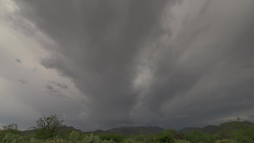 A dramatic zoom and tilt-up reveals ominous dark storm clouds gathering over a green desert mountain landscape