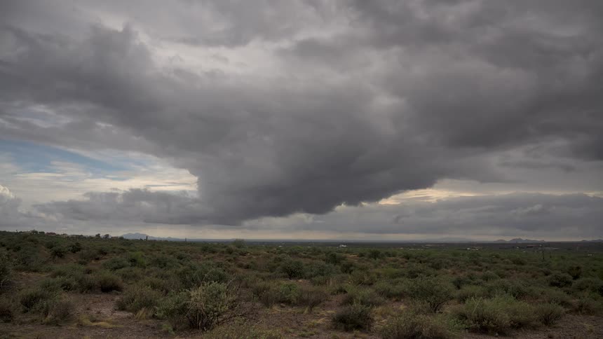Ominous grey storm clouds slowly drift over a vast, arid desert landscape
