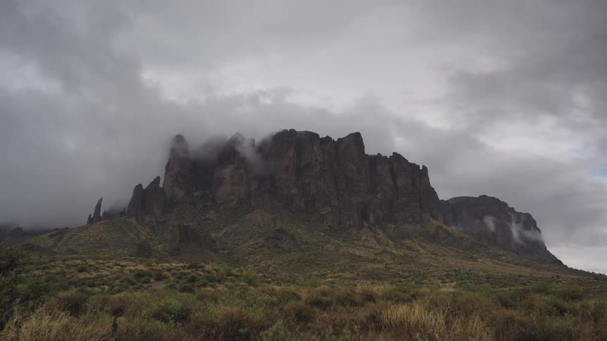 Heavy fog and dramatic storm clouds move across the peaks of a rugged mountain range