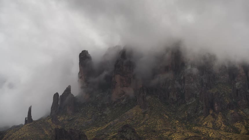 Thick, moody clouds and fog roll across the jagged peaks of a majestic mountain range