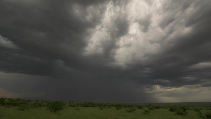 A dramatic time-lapse shows immense and powerful dark storm clouds churning and moving across a vast green landscape