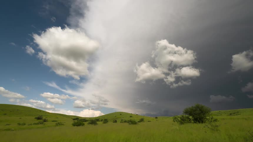A time-lapse of a massive storm front with dark, turbulent clouds encroaching on a sunny, blue sky over rolling green hills