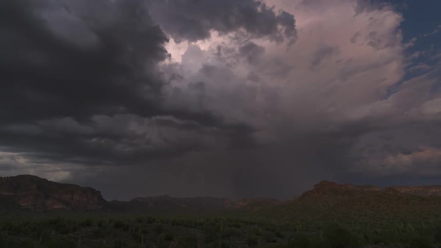 A dramatic lightning storm rages over a desert mountain landscape as day turns to night