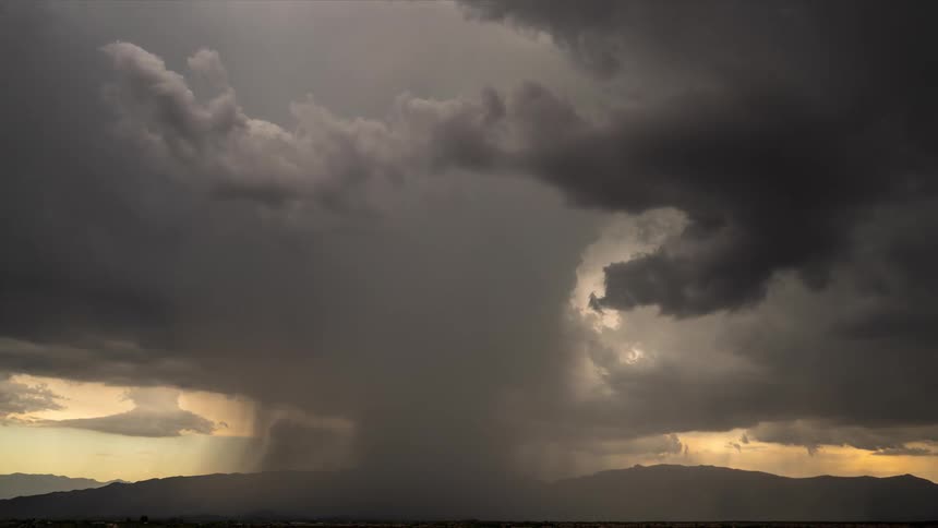 Dramatic time-lapse of a powerful rainstorm with a concentrated downpour over a mountain range as sun rays pierce through the dark clouds