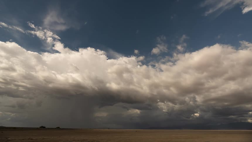 Dramatic storm clouds gather and release rain over a vast, empty desert plain