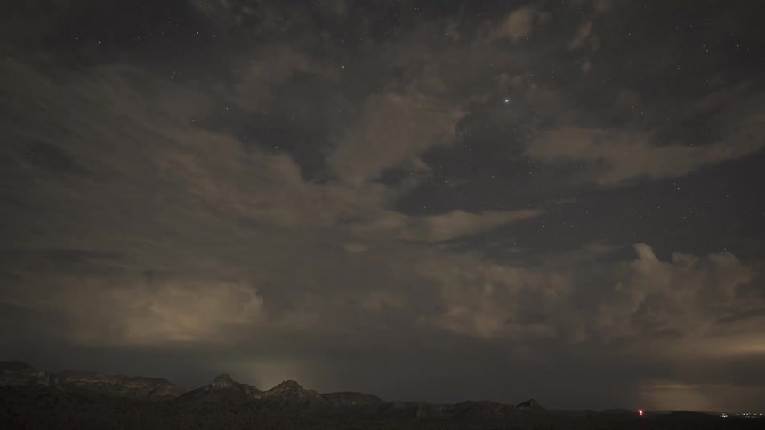 Stars peek through moving clouds as a dramatic lightning storm rages over a mountain range in this night time-lapse