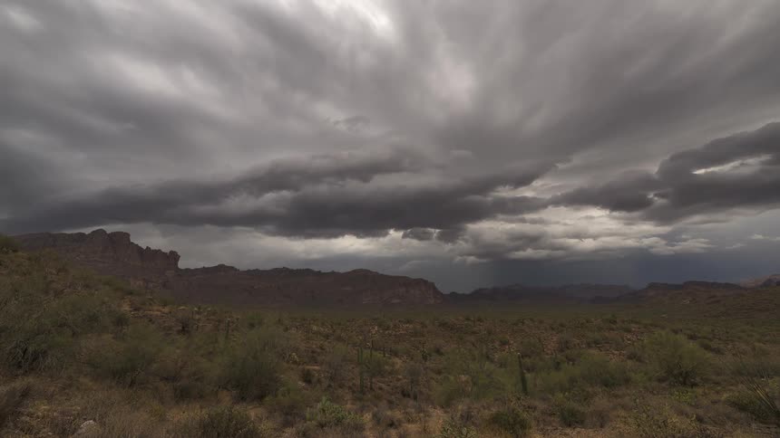 A dramatic time-lapse of ominous storm clouds gathering and swirling over a vast desert mountain landscape
