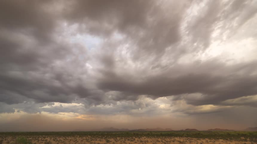 A dramatic time-lapse shows stormy clouds swirling over a vast desert landscape as the sky begins to clear at sunset