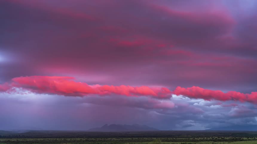 A dramatic timelapse captures storm clouds rolling over a vast landscape, illuminated by a brilliant pink sunset