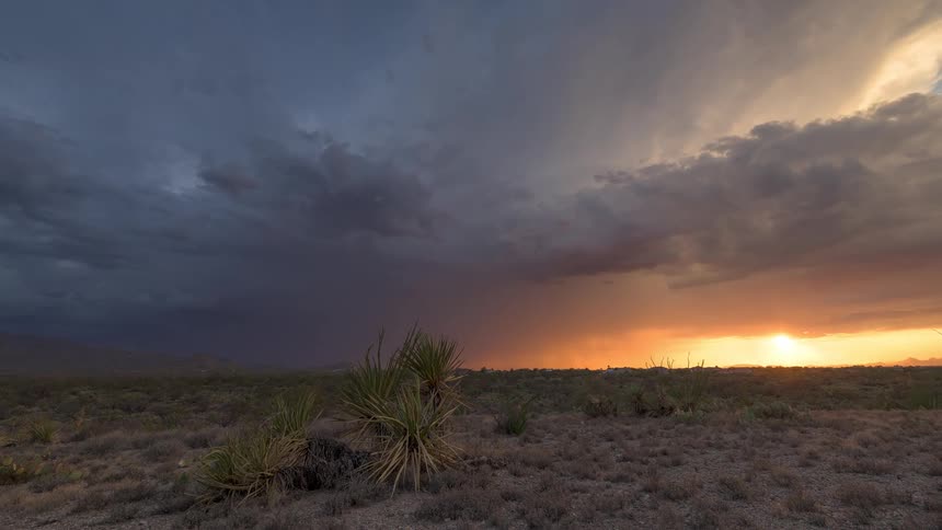 A stunning timelapse captures the beautiful contrast between a dark rainstorm and a vibrant golden sunset over a desert landscape
