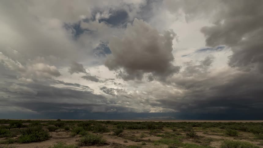 Dramatic storm clouds gather and darken in a time-lapse over a wide, open desert landscape