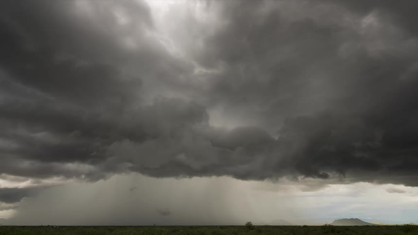 A time-lapse of a powerful thunderstorm with dark, churning clouds releasing a heavy downpour over a wide, flat landscape