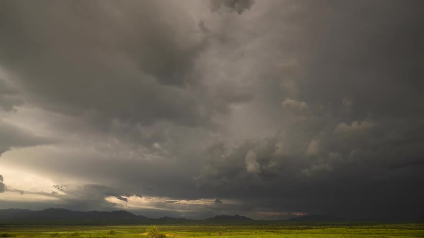 A dramatic time-lapse captures ominous storm clouds swirling over a vast, vibrant green grassland as sunlight breaks through the darkness