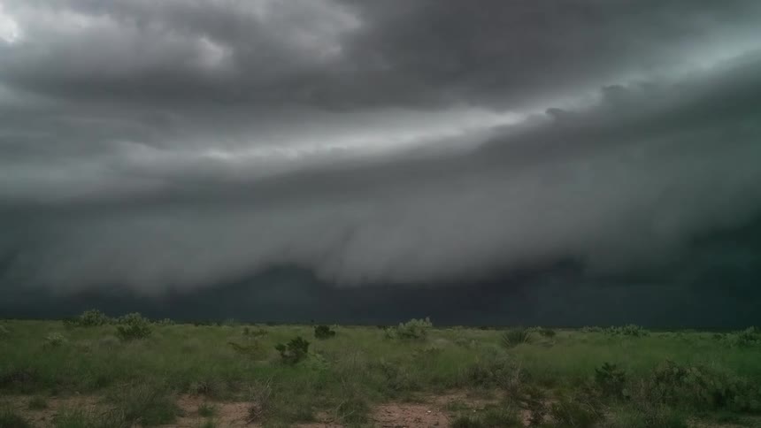 A dramatic time-lapse of a massive, dark storm front with turbulent shelf clouds advancing across a vast, grassy plain