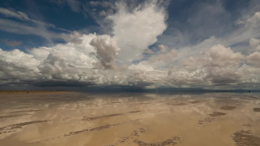 A surreal time-lapse shows a dramatic cloudy sky perfectly reflected on the calm, wet surface of a vast salt flat