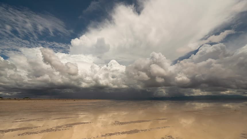 A surreal time-lapse shows dramatic storm clouds moving across the sky and reflecting perfectly in the still water of a vast, flooded salt flat