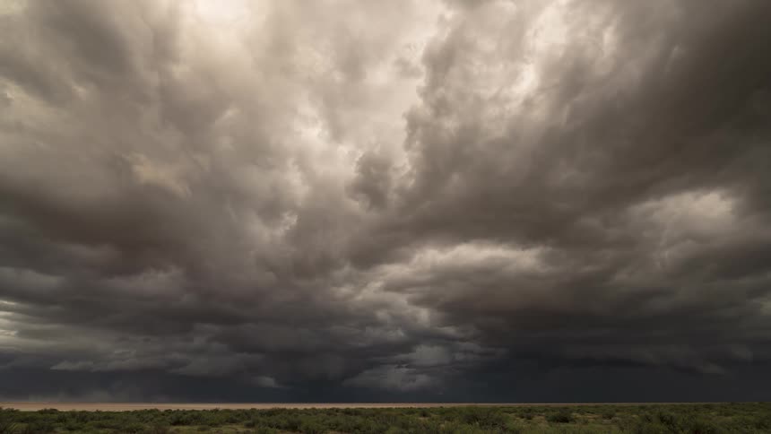 A dramatic time-lapse captures dark, turbulent storm clouds gathering and moving over a vast, arid plain as rain begins to fall