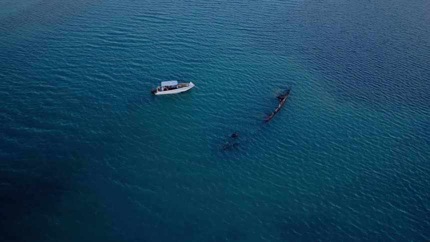 Static aerial shot reveals a submerged shipwreck in the tranquil turquoise sea, with a small boat anchored nearby