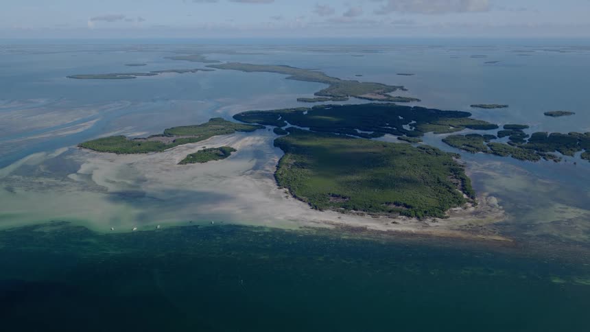 A static wide aerial view of a tropical archipelago with lush green mangrove islands surrounded by turquoise water and white sandbars