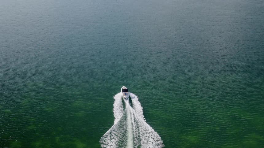 Aerial view of a white motorboat cruising through beautiful clear green water, leaving a prominent wake behind it