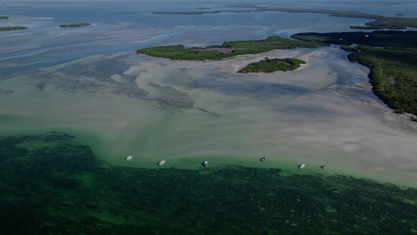 A static aerial view shows a fleet of boats anchored along a stunning sandbar in the tropical waters of the Florida Keys