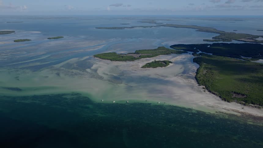 High aerial static shot of a beautiful tropical archipelago with clear turquoise waters, sandbars, mangrove islands, and several boats anchored in the shallows