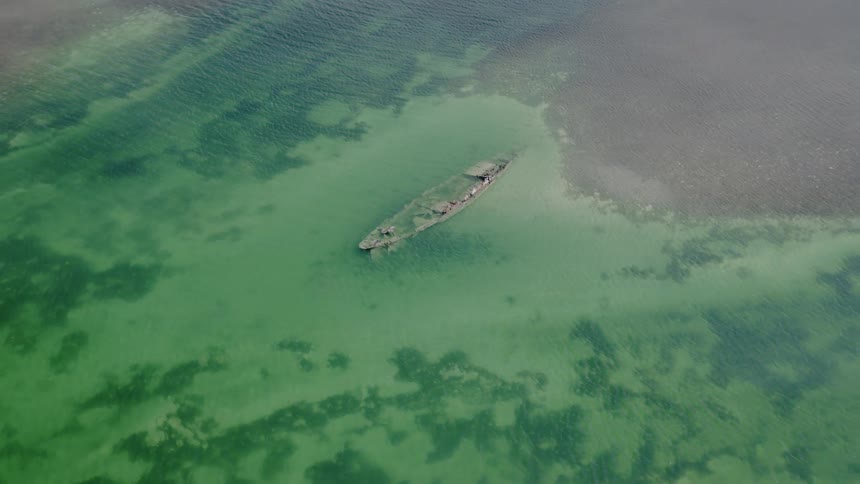 An aerial view of the forgotten wreckage of a ship resting peacefully beneath the clear, green ocean waters