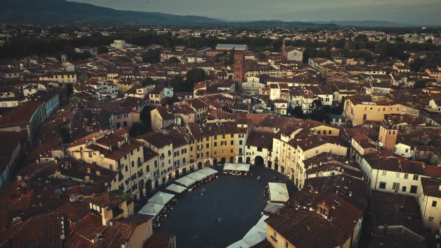 A stunning aerial time-lapse captures the transition from dusk to night over the iconic Piazza dell'Anfiteatro in Lucca, Italy