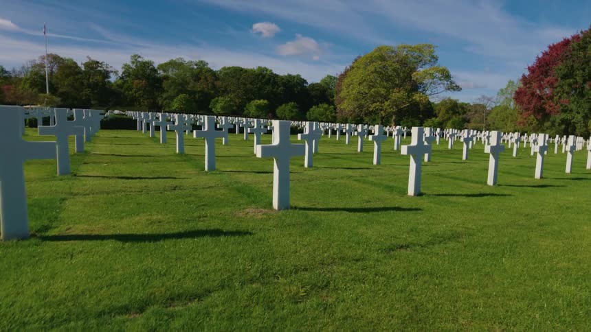 A somber Dutch angle shot slowly rotates over rows of white crosses at a military cemetery on a sunny day