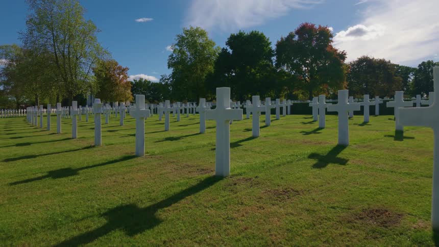 A slow dolly shot glides through rows of pristine white crosses at a military cemetery on a sunny day