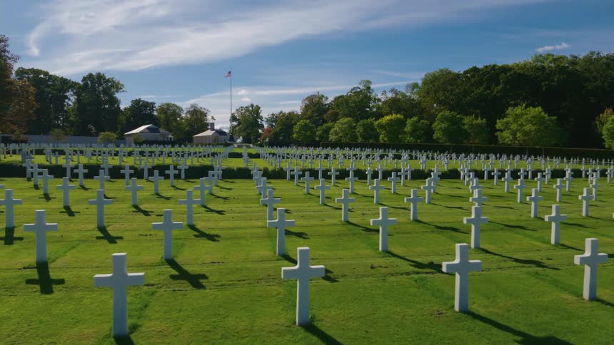A slow pan reveals rows of white crosses at the Normandy American Cemetery and Memorial on a sunny day
