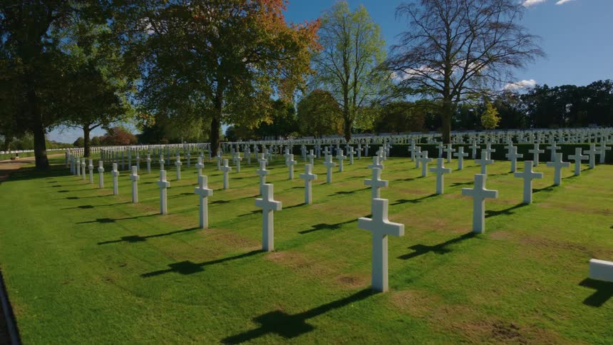 Sunlight casts long shadows from the white cross grave markers at a serene military cemetery surrounded by autumn trees