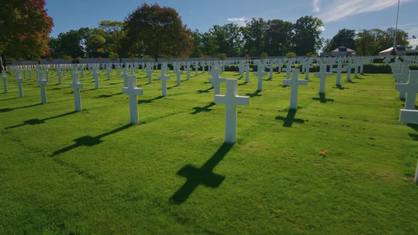 Rows of white crosses cast long shadows across the perfectly manicured green lawn of a military cemetery on a bright sunny day